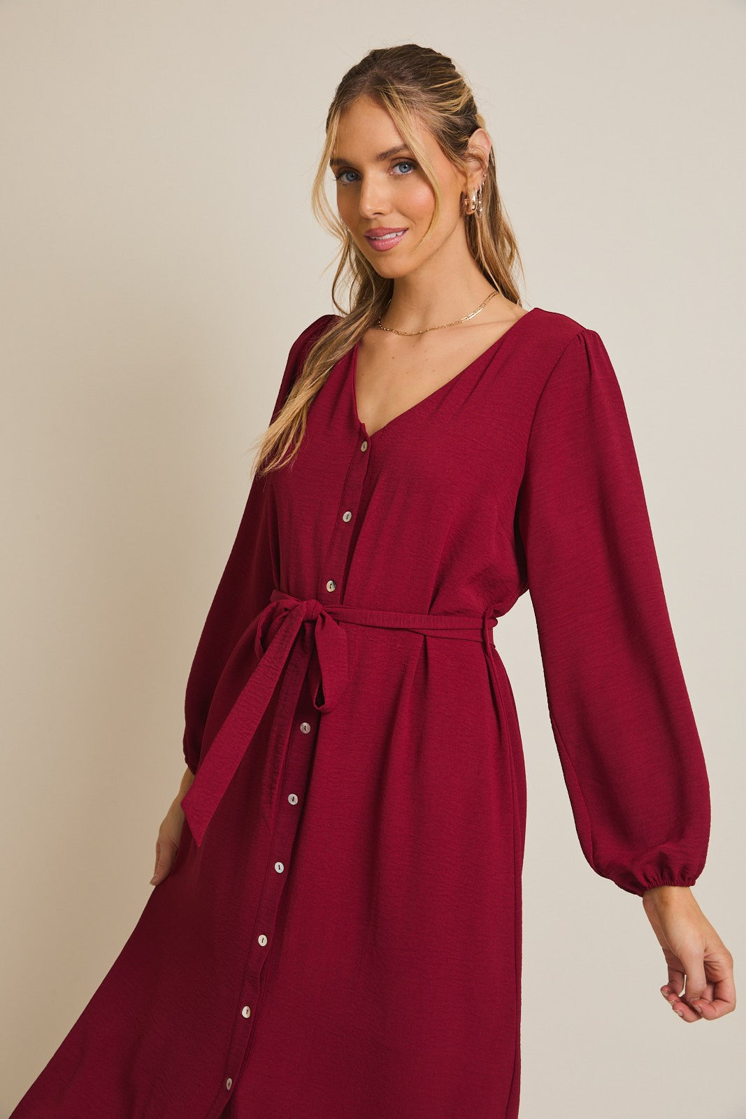 woman wearing a burgundy button-up dress with a v-neck and long puff sleeves, cinched at the waist with a tie belt