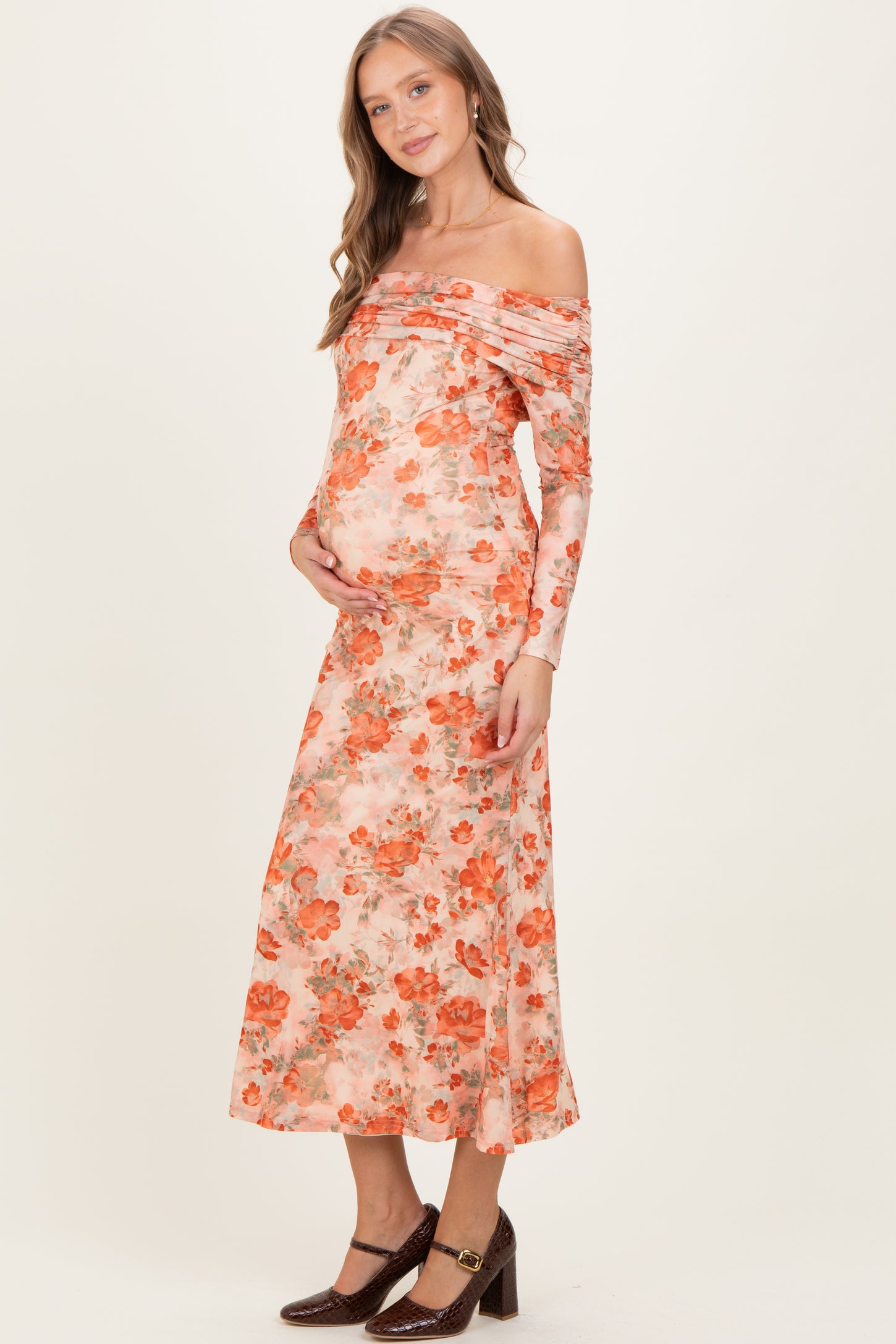 woman wearing a floral off-the-shoulder maternity dress and holding her baby bump