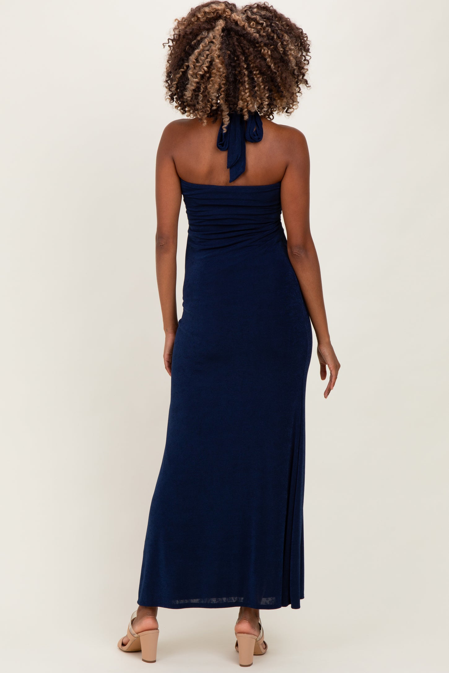 woman wearing a navy blue strapless maternity maxi dress with a halter neck and gathering details in the back