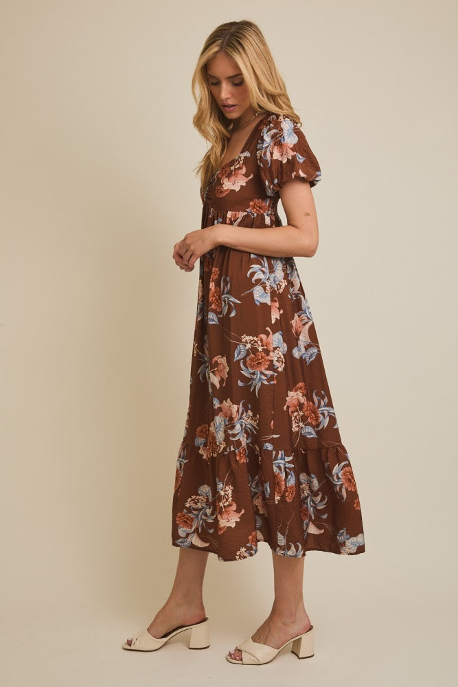 woman wearing a brown floral maxi dress with puff sleeves and a tiered skirt, standing sideways
