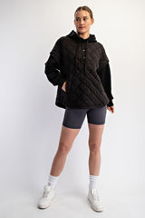 woman wearing a black quilted pullover hoodie with buttons, paired with gray bike shorts and white sneakers