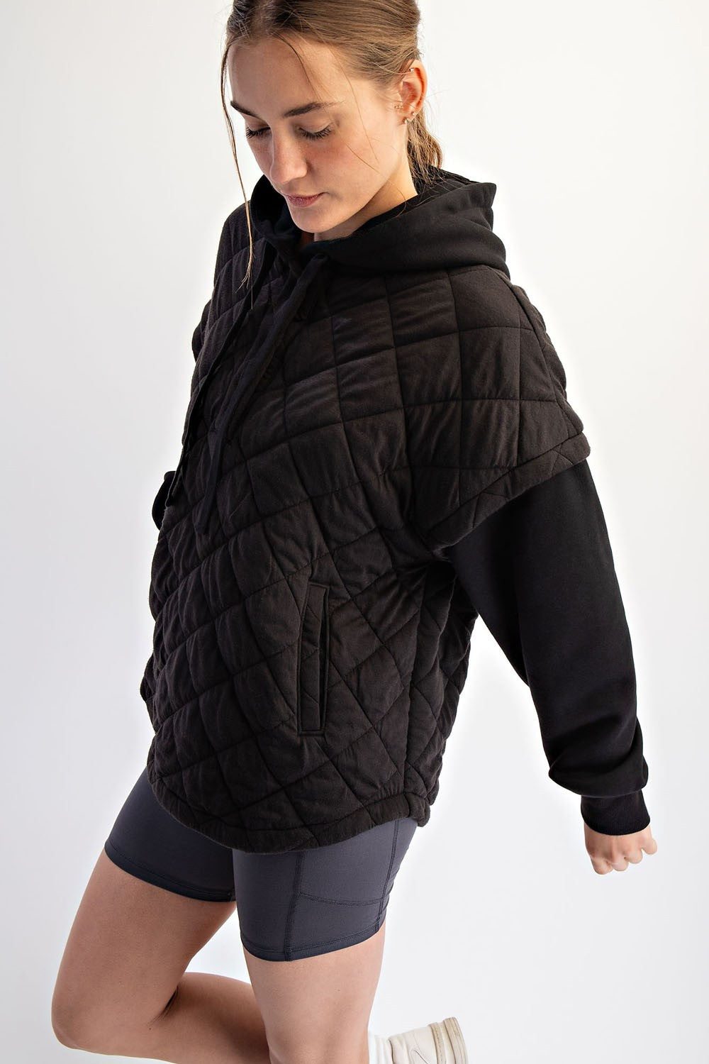 woman wearing a black quilted oversized hoodie with short sleeves and side pockets paired with gray shorts