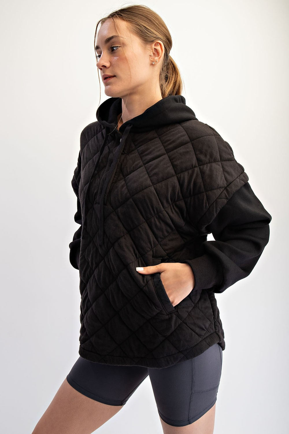 woman wearing a black quilted hoodie with a front pocket and a relaxed fit, paired with gray cycling shorts