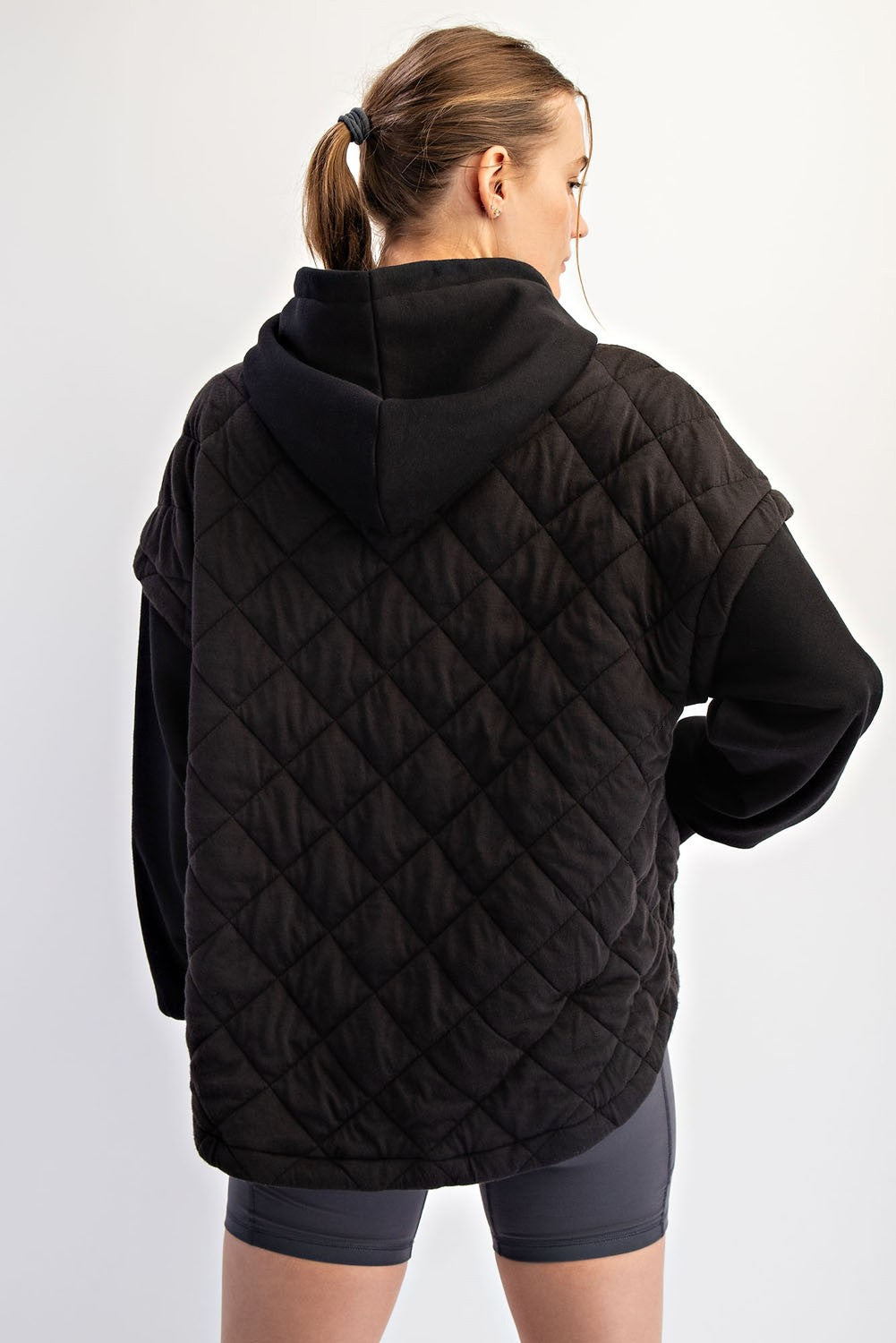 woman wearing a black quilted oversized hoodie with a hood and short sleeves, showing the back view