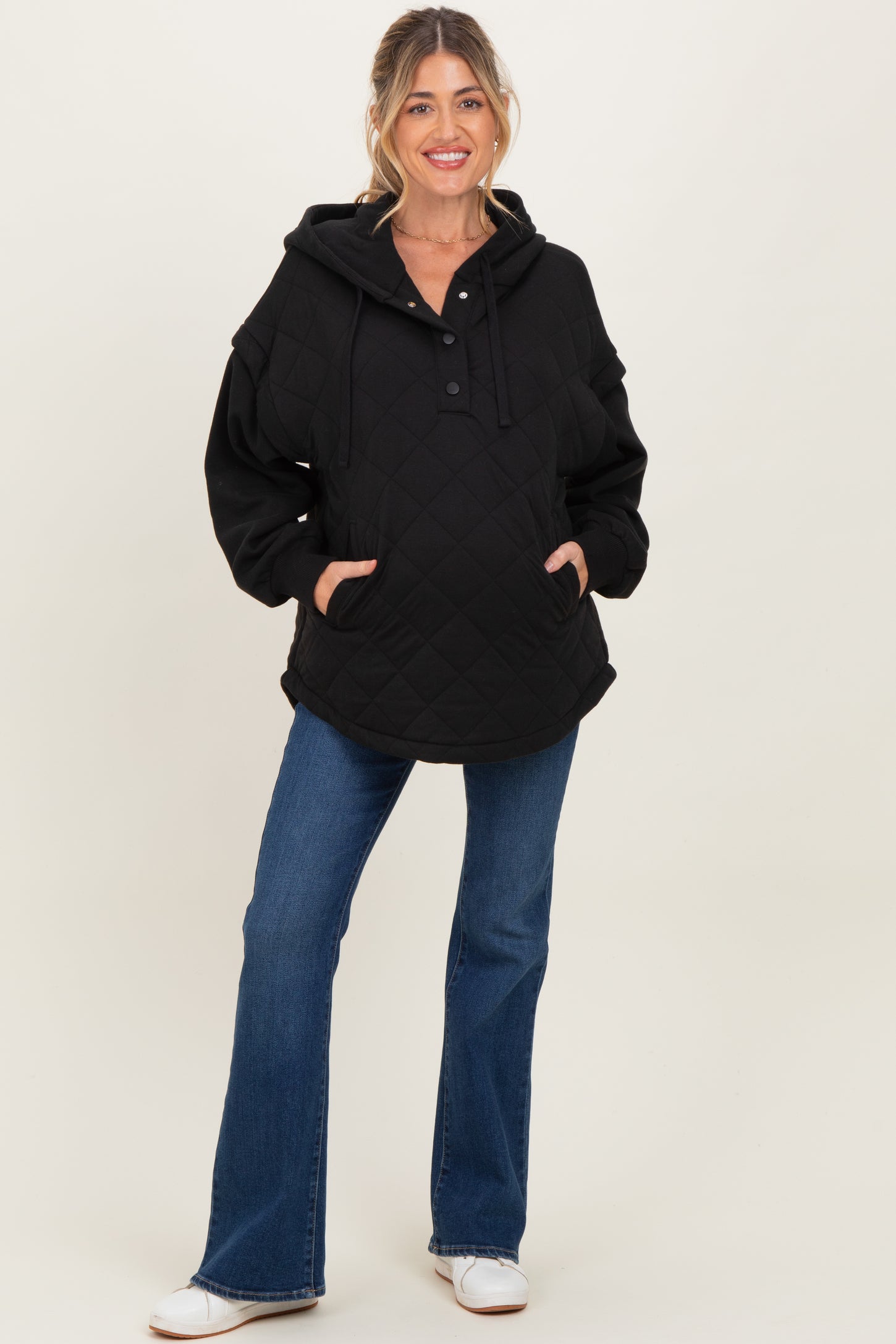 woman wearing a black quilted maternity hoodie with a front pocket and button detail, paired with blue flared jeans