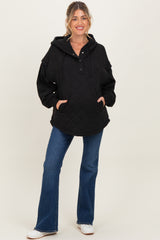 woman wearing a black quilted maternity hoodie with a front pocket and button detail, paired with blue flared jeans