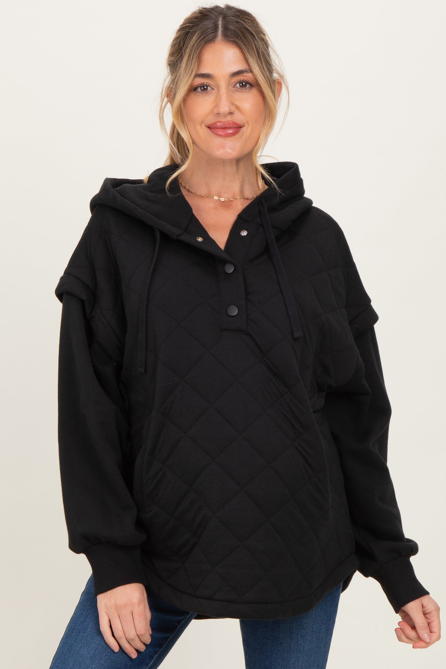 woman wearing a black quilted maternity hoodie with a henley neckline and oversized fit, showing a baby bump