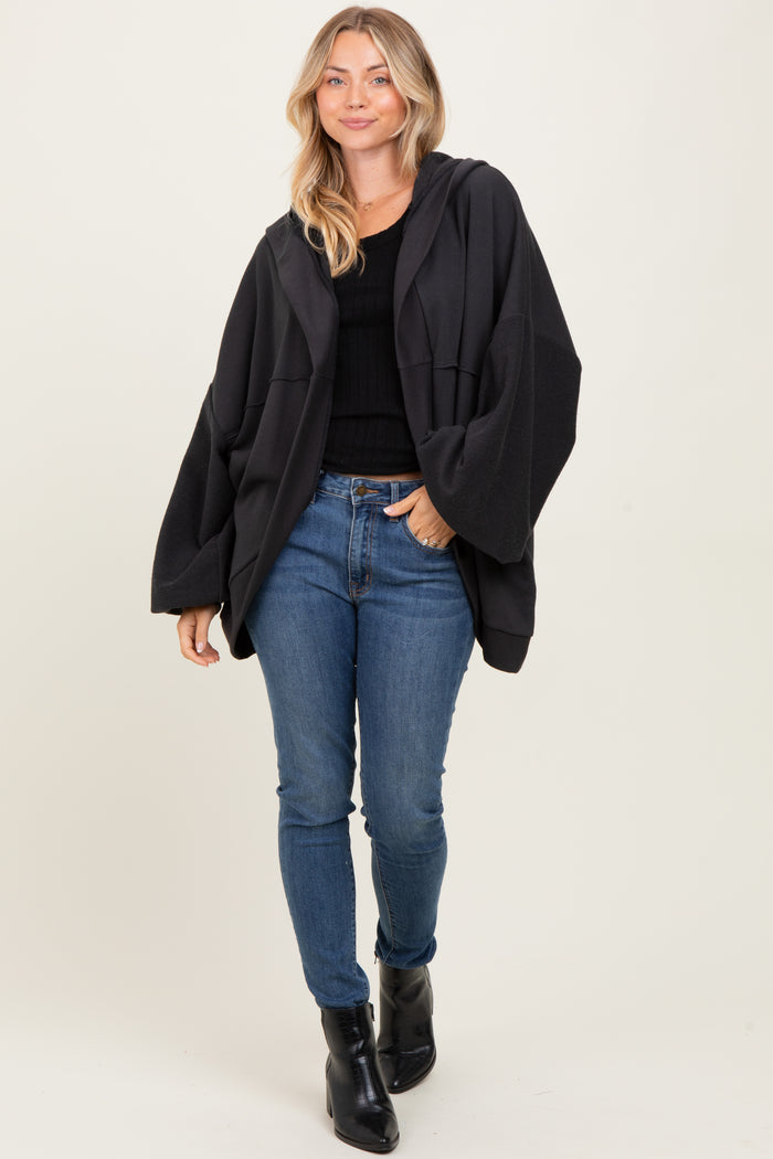 woman wearing a black oversized hoodie over a fitted black top and blue skinny jeans, with black ankle boots