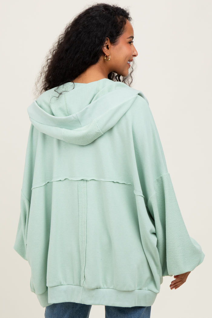 woman wearing a light green oversized maternity hoodie with a hood and relaxed fit, showing her back
