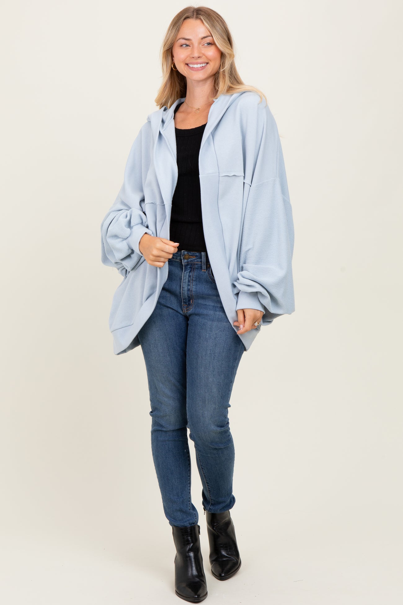 woman wearing a light blue oversized hoodie and black top, paired with blue jeans and black ankle boots