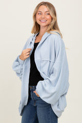 woman wearing a light blue oversized hoodie with a front pocket and black top underneath, smiling against a neutral background