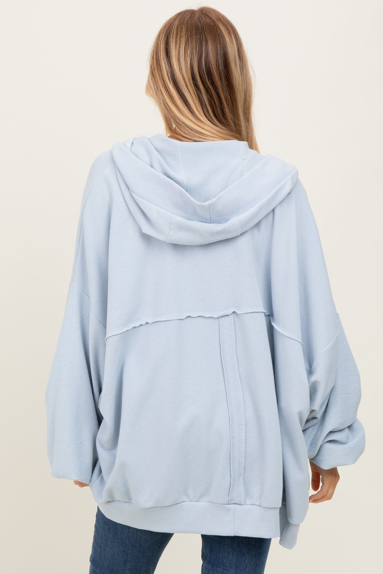 woman wearing a light blue oversized hoodie with a relaxed fit and a hood, seen from the back in a casual pose