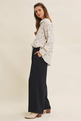 woman wearing a cream floral print long sleeve shirt and navy wide-leg trousers with a casual pose