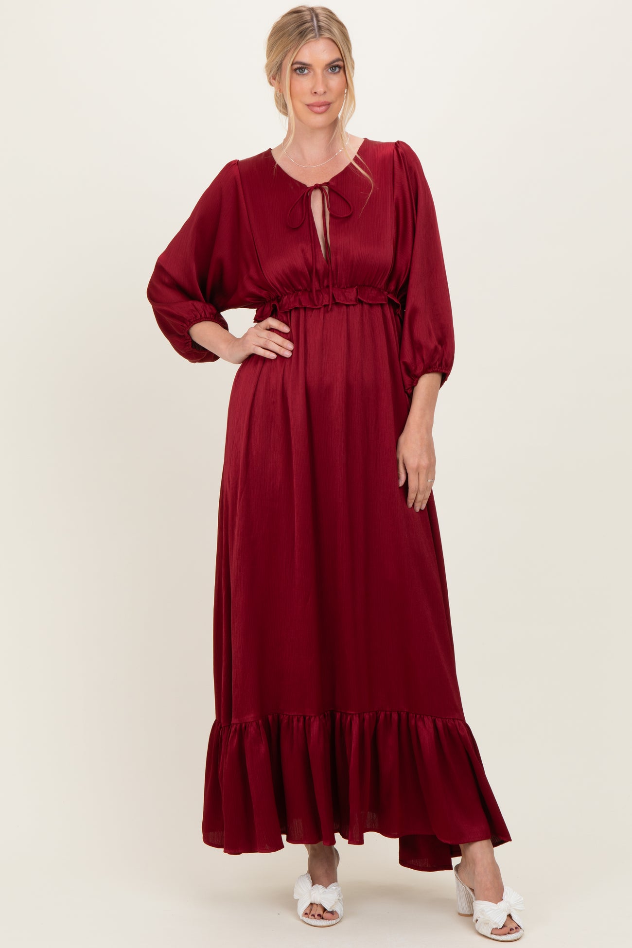 woman wearing a burgundy maxi dress with puff sleeves and a ruffled hem, styled with a tie neckline and white sandals