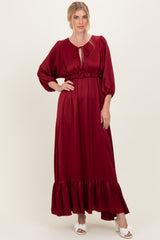 woman wearing a burgundy maxi dress with puff sleeves and a ruffled hem, styled with a tie neckline and white sandals