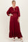woman wearing a burgundy maxi dress with puff sleeves and a ruffled hem, styled with a tie neckline and white sandals