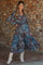 woman wearing a paisley print maternity maxi dress with long sleeves and tiered skirt, posing in front of a stone wall