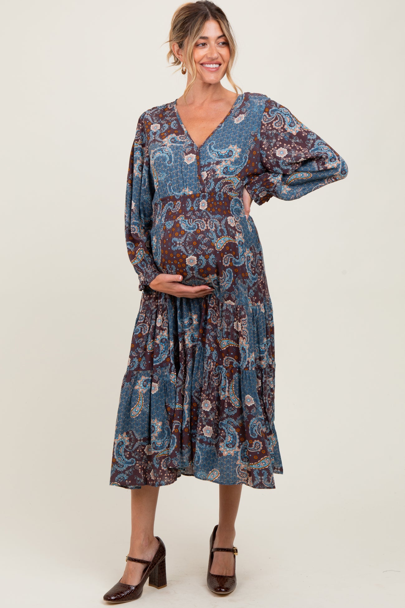 woman wearing a blue paisley print maternity dress with a v-neckline and bell sleeves, holding her baby bump