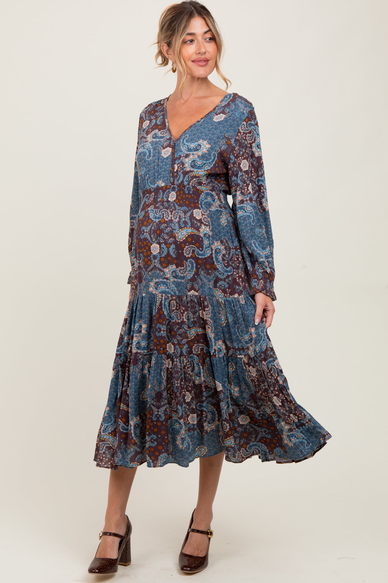 woman wearing a paisley print blue and brown maternity dress with a v-neck and tiered hem, showcasing her baby bump