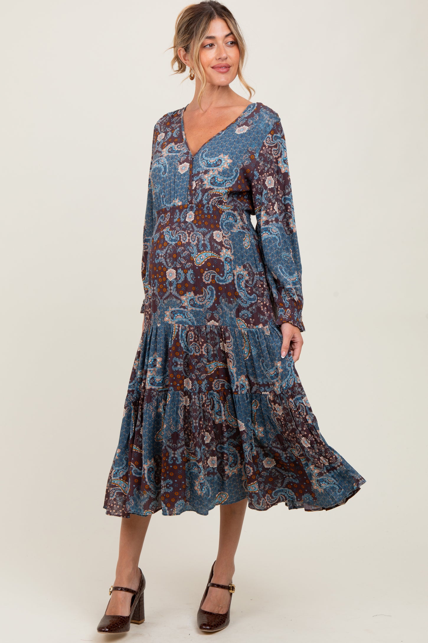 woman wearing a paisley print blue and brown maternity dress with a v-neck and tiered hem, showcasing her baby bump