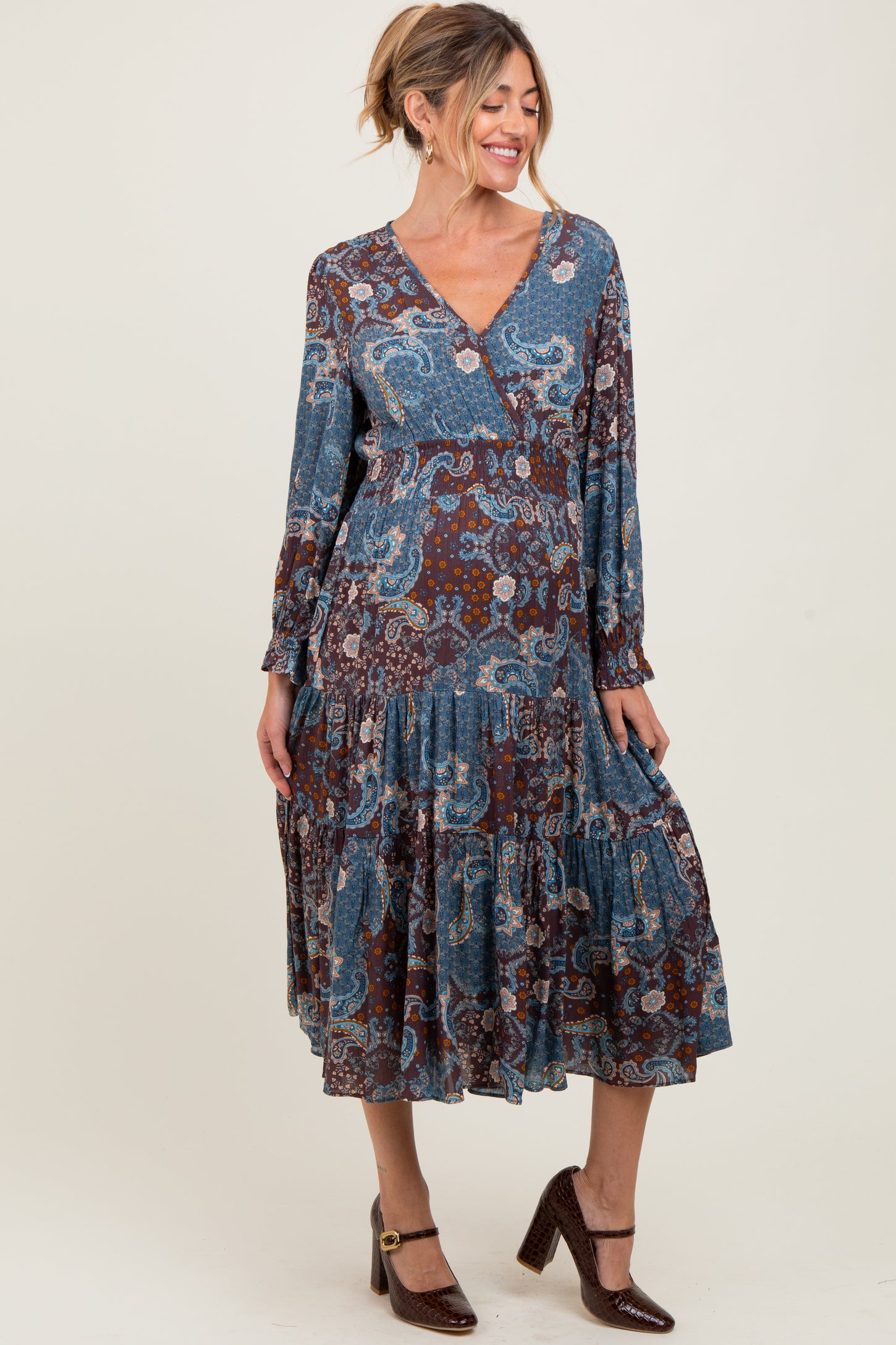woman wearing a blue and brown paisley print maternity dress with long sleeves and a tiered skirt, showing her baby bump