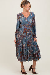 woman wearing a blue and brown paisley print maternity dress with long sleeves and a tiered skirt, showing her baby bump