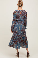 woman wearing a floral patterned blue maternity dress with long sleeves and ruffled hem, showing a slight baby bump from the back