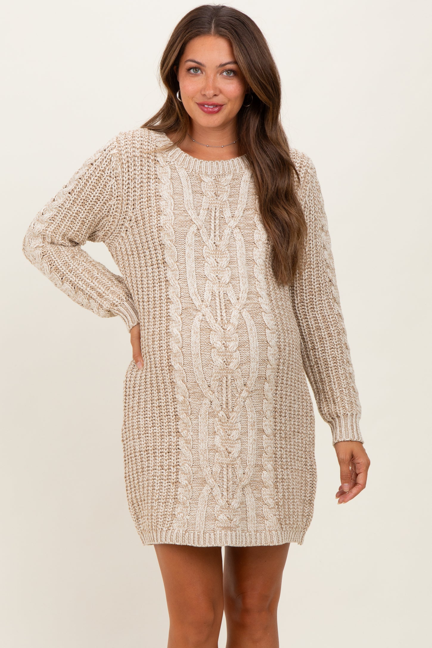 woman wearing a beige cable-knit maternity sweater dress with long sleeves and a relaxed fit, showcasing her baby bump