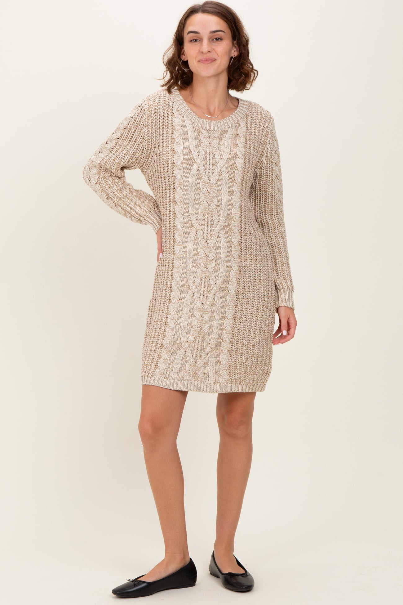 woman wearing a beige knitted sweater dress with cable knit pattern and long sleeves, standing with a smile