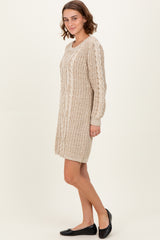 woman wearing a beige knitted sweater dress with cable-knit details and long sleeves, paired with black flats