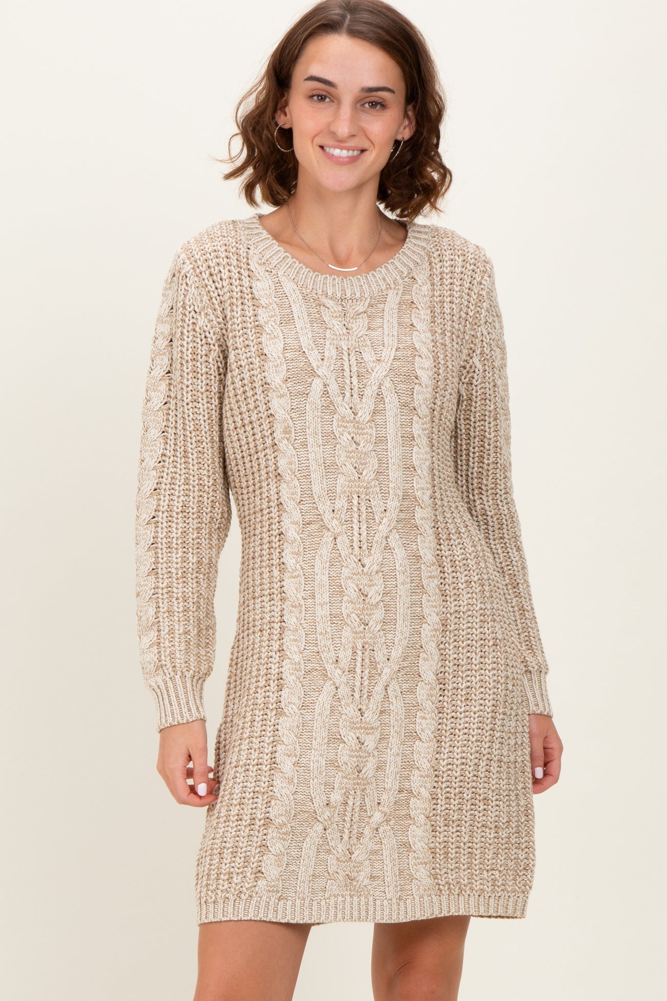 woman wearing a beige cable knit sweater dress with long sleeves and a relaxed fit