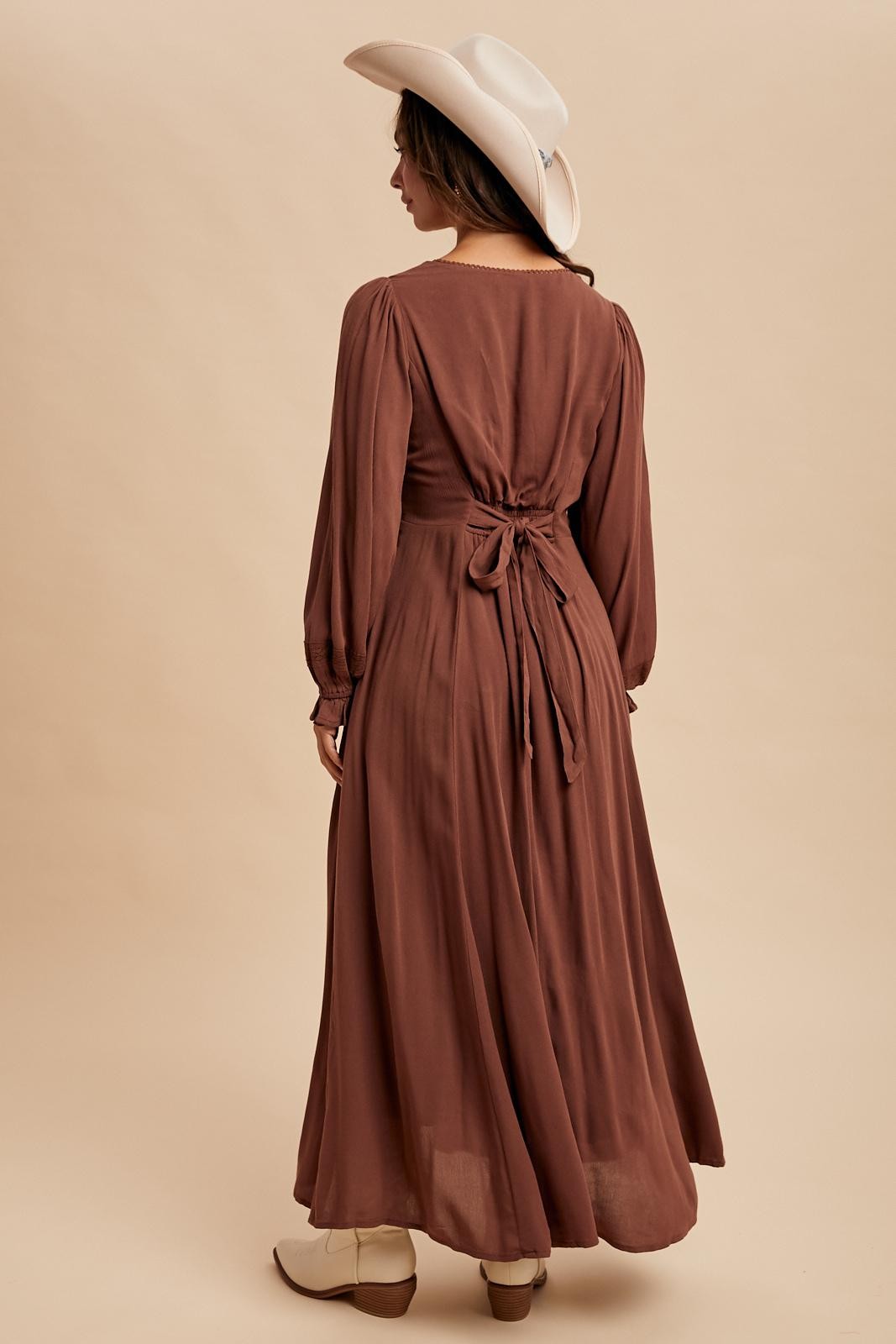 woman wearing a brown long sleeve maxi dress with tie back detail and a white cowboy hat