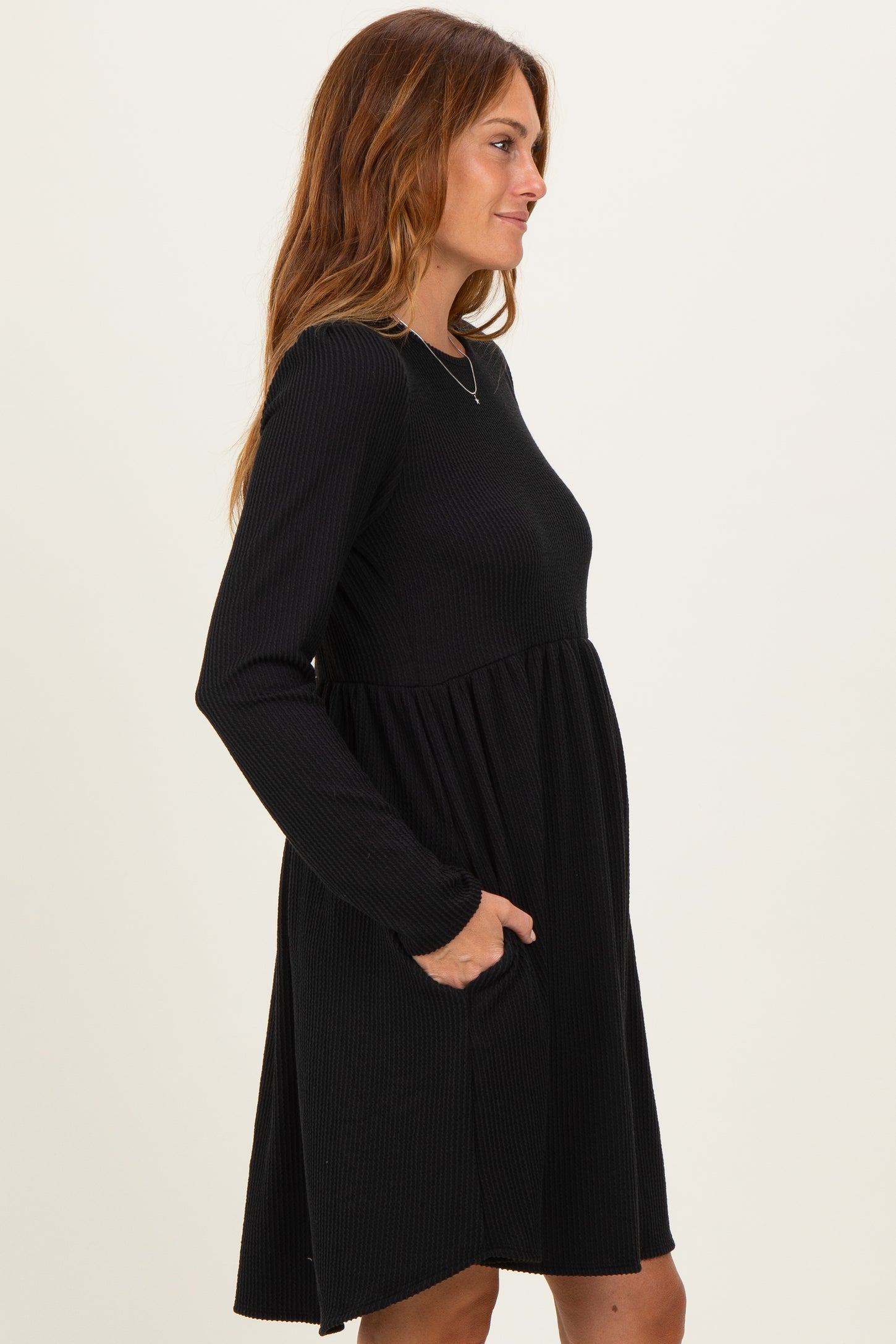 woman wearing a black long sleeve dress with a ribbed texture and pockets, shown from the side
