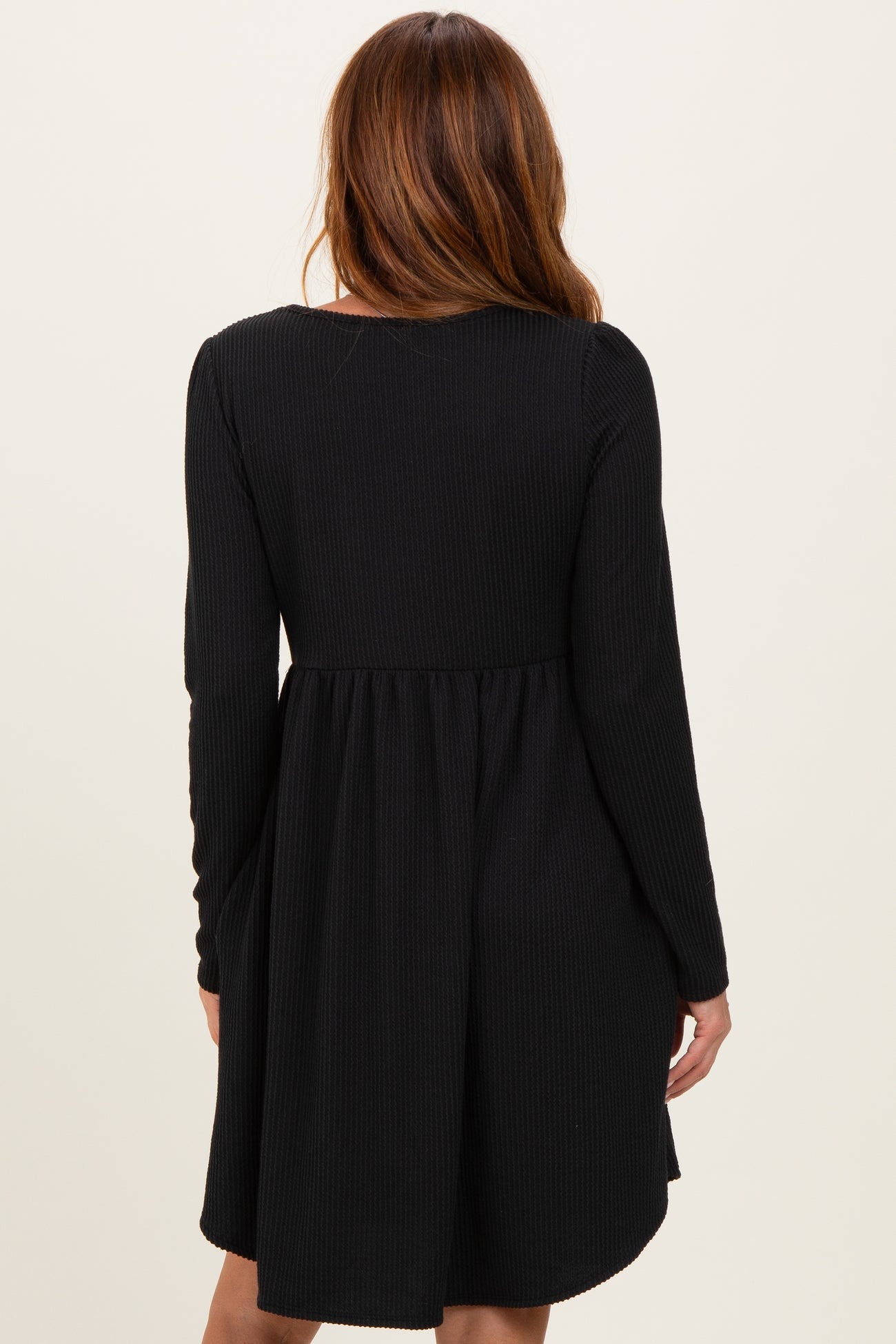 woman wearing a black ribbed long sleeve dress with a flared skirt, viewed from the back