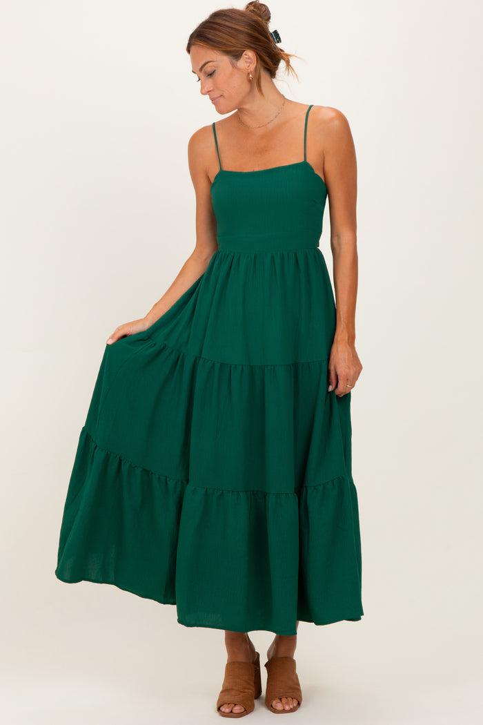 woman wearing a dark green tiered maxi dress with spaghetti straps and a fitted bodice, holding the skirt gently