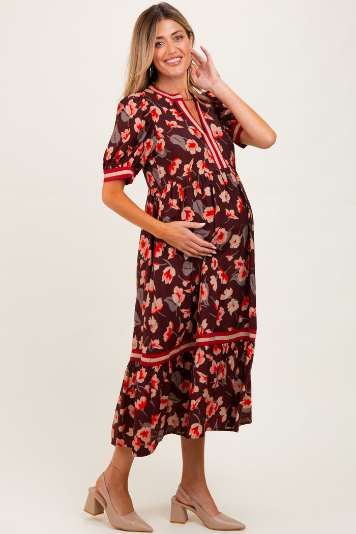 woman wearing a brown floral maternity dress with short sleeves and a tiered skirt, holding her baby bump
