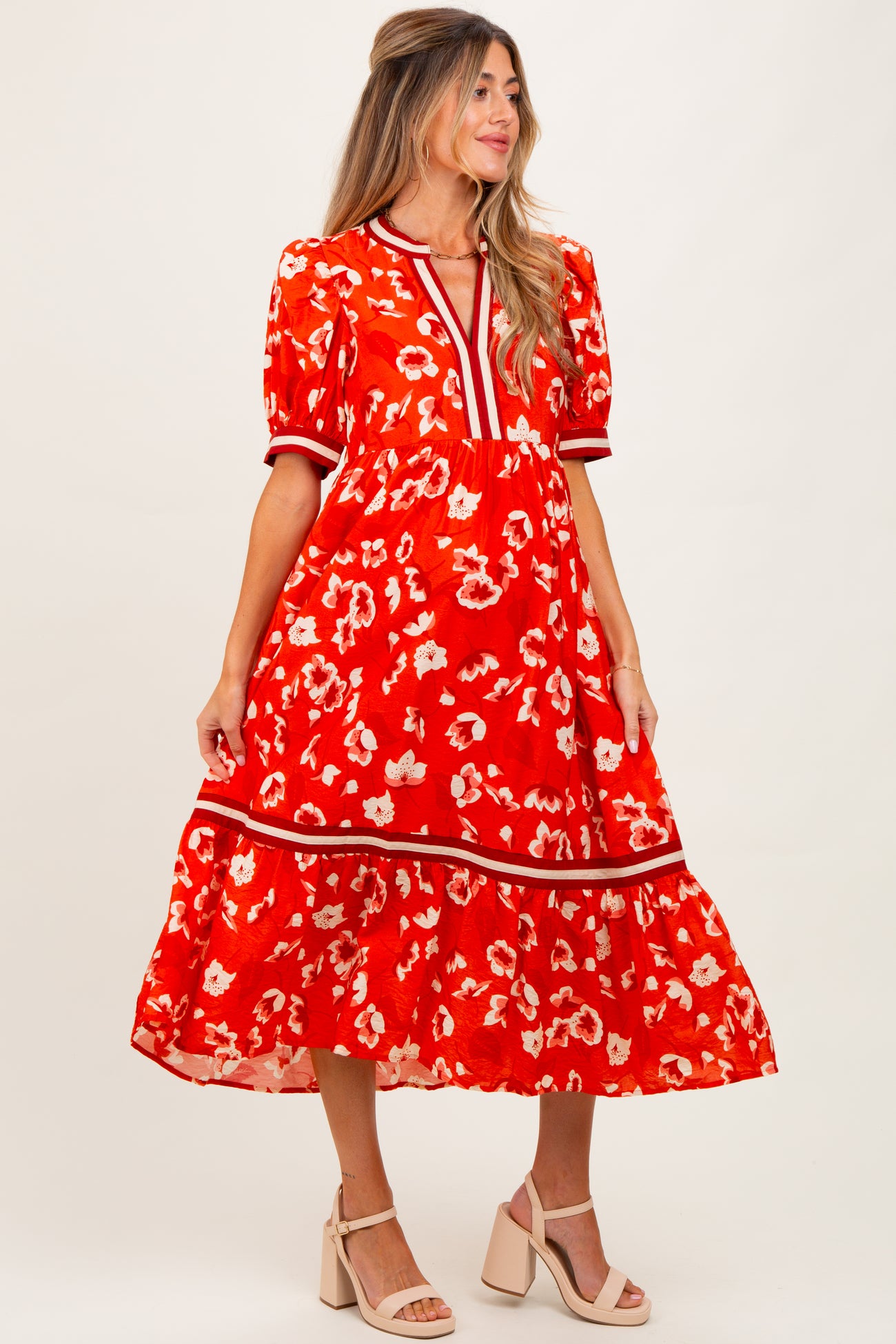 woman wearing a red floral maternity dress with puff sleeves and a tiered skirt, standing against a plain background