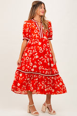 woman wearing a red floral maternity dress with puff sleeves and a tiered skirt, standing against a plain background