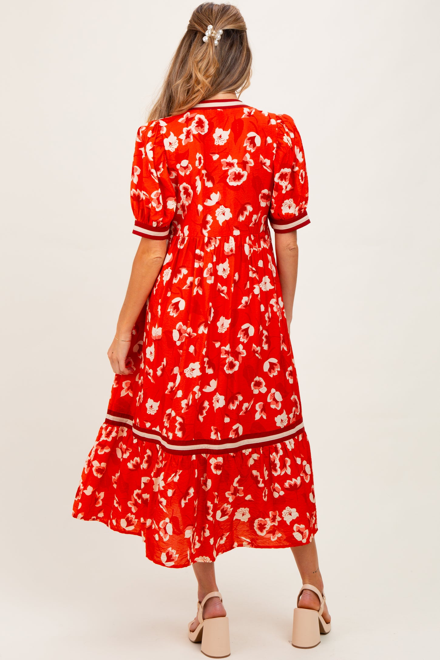 woman wearing a red floral maternity dress with a tiered skirt and puff sleeves, showing a baby bump from behind