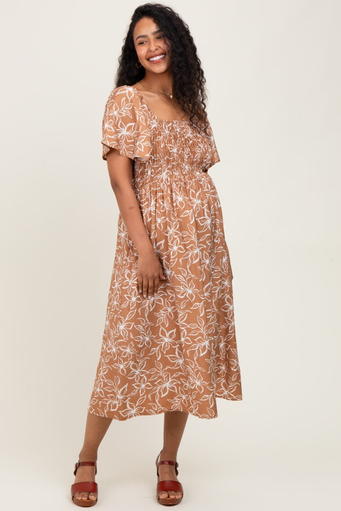 woman wearing a brown floral print maternity dress with short sleeves and a smocked bodice, showing her baby bump