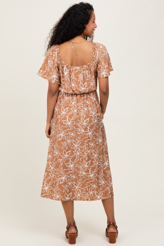 woman wearing a brown floral maternity dress with short flutter sleeves and a tie waist, standing with her back to the camera