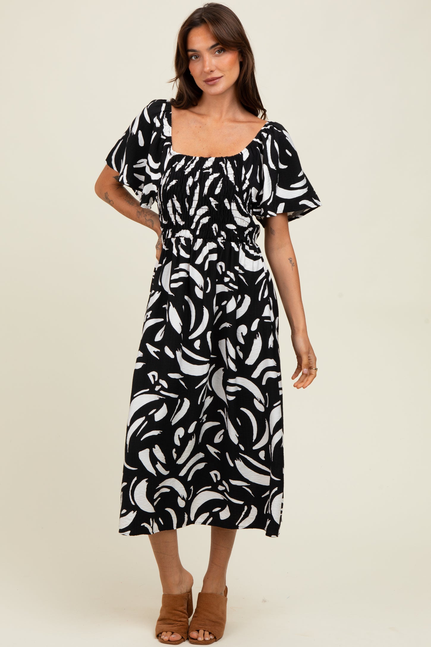 woman wearing a black and white abstract print midi dress with short flutter sleeves and a smocked waist