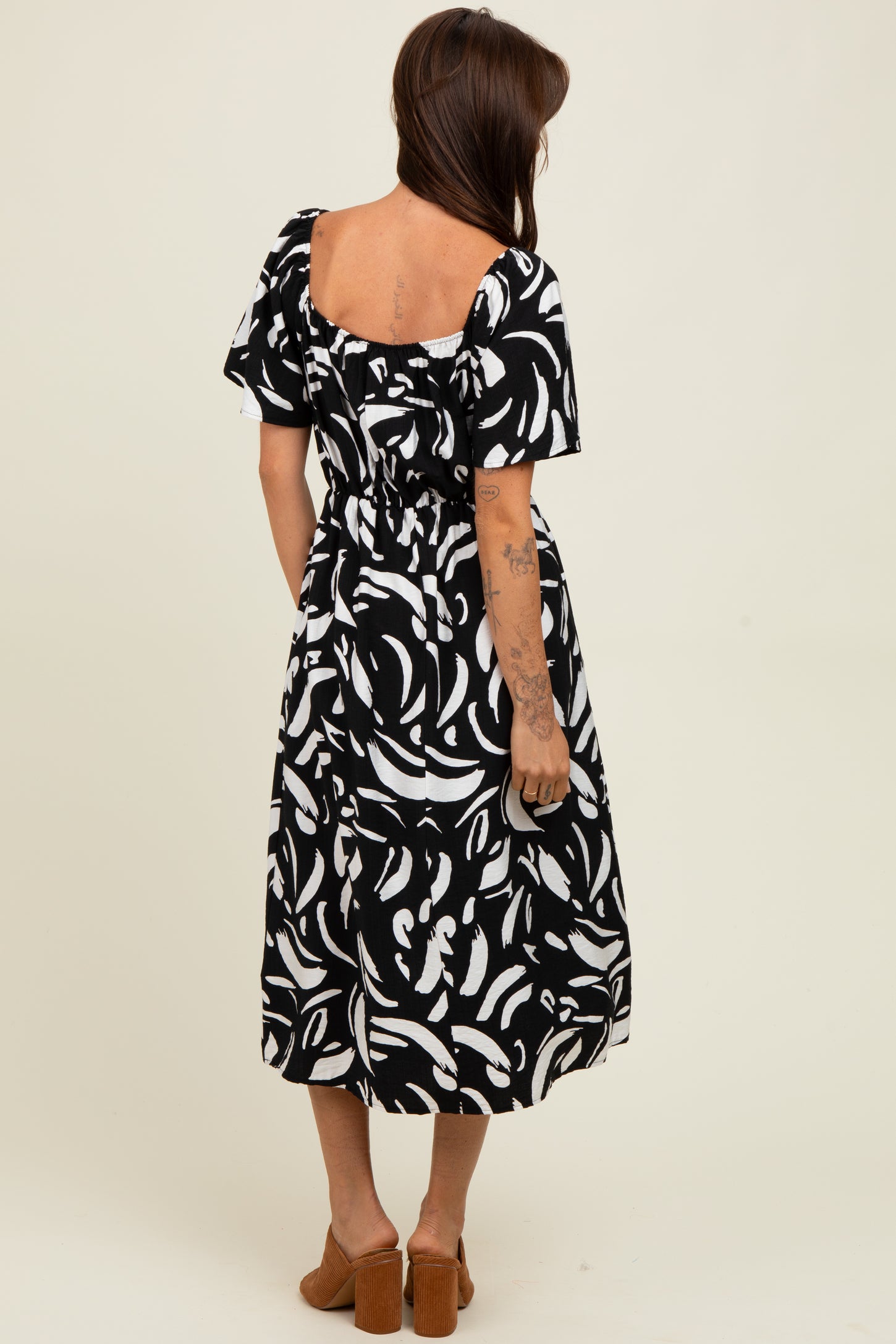 woman wearing a black and white patterned midi dress with short sleeves and a fitted waist, viewed from the back