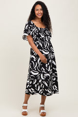 woman wearing a black and white patterned maternity dress with a smocked waist and flutter sleeves, holding her baby bump
