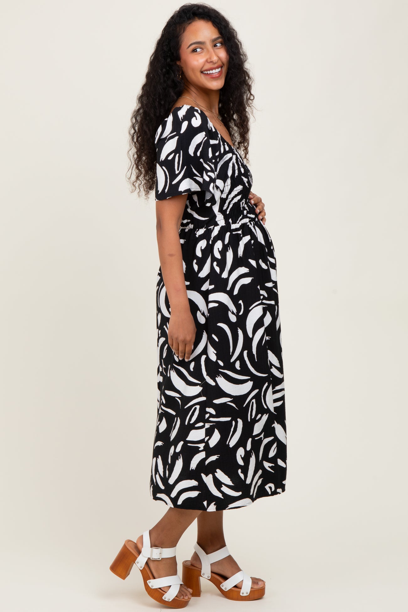 woman wearing a black and white patterned maternity dress, smiling with a visible baby bump and standing in profile