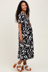 woman wearing a black and white patterned maternity dress, smiling with a visible baby bump and standing in profile