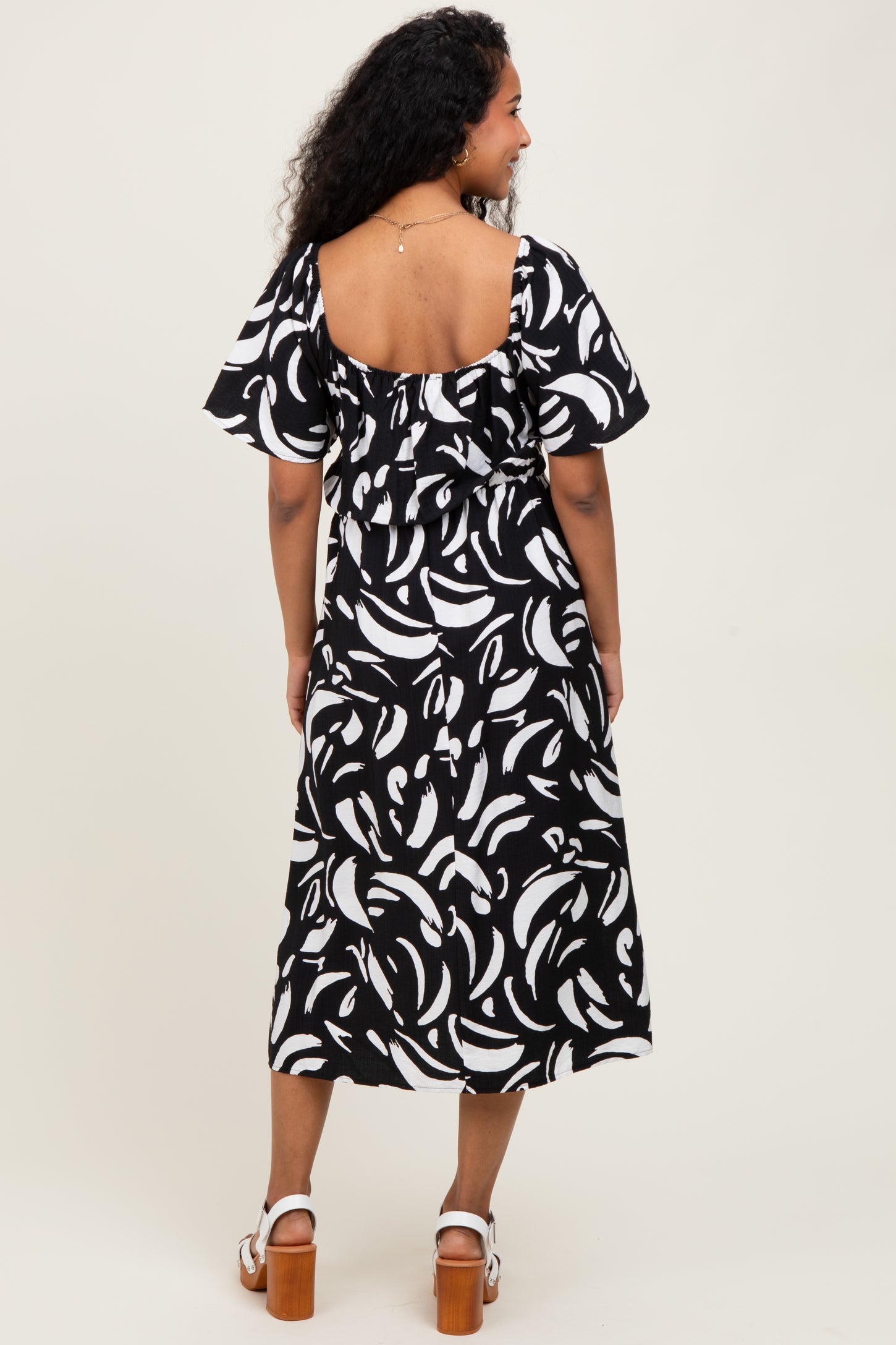 woman wearing a black and white patterned maternity dress with flutter sleeves and a ruffled back.