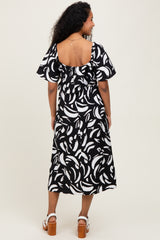 woman wearing a black and white patterned maternity dress with flutter sleeves and a ruffled back.
