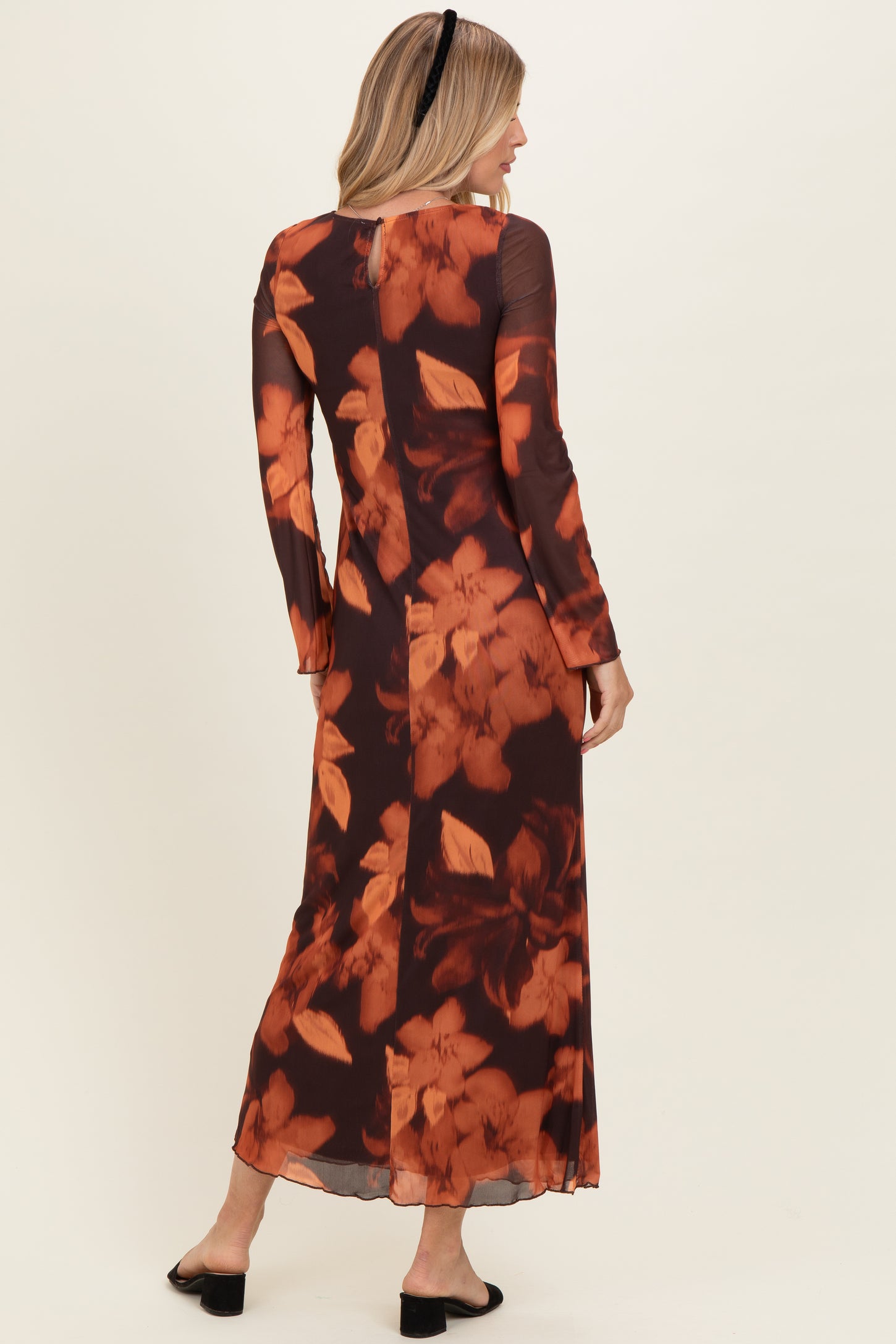 woman wearing a long sleeve floral maxi dress in shades of brown and orange, back view