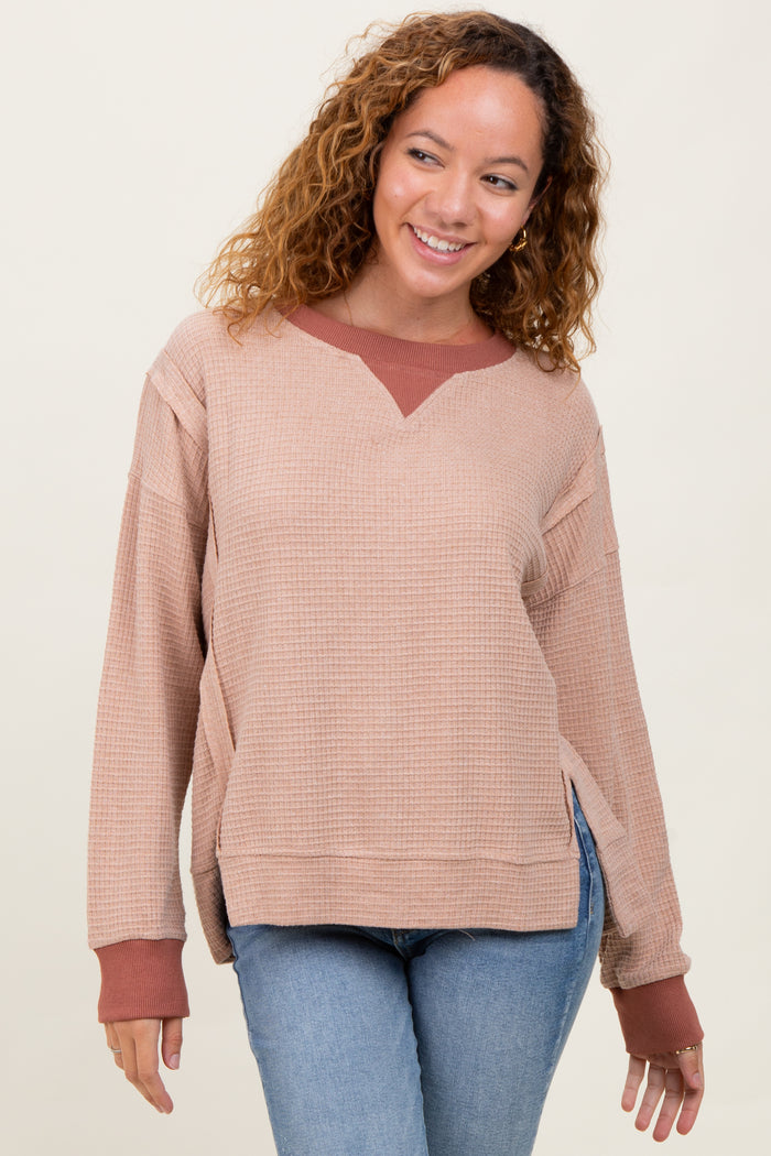 woman wearing a beige oversized waffle knit sweater with a maroon collar and side slits, paired with blue jeans